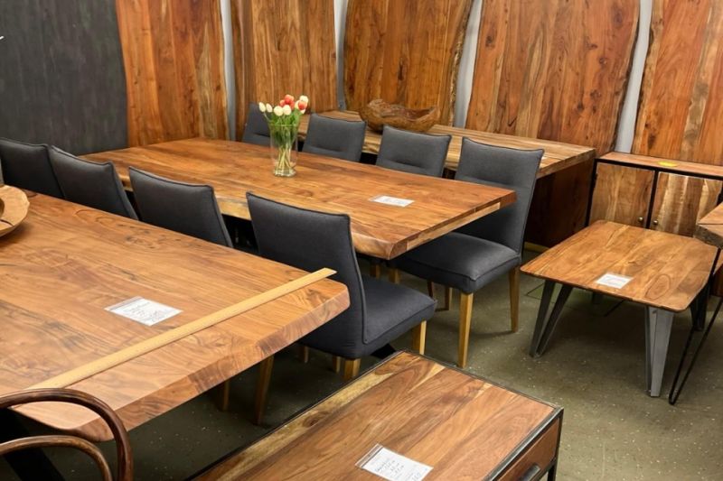 Ausstellung mit mehreren Massivholztischen und passenden Stühlen sowie großen Holzplatten an der Wand in einem Geschäft für Holztische